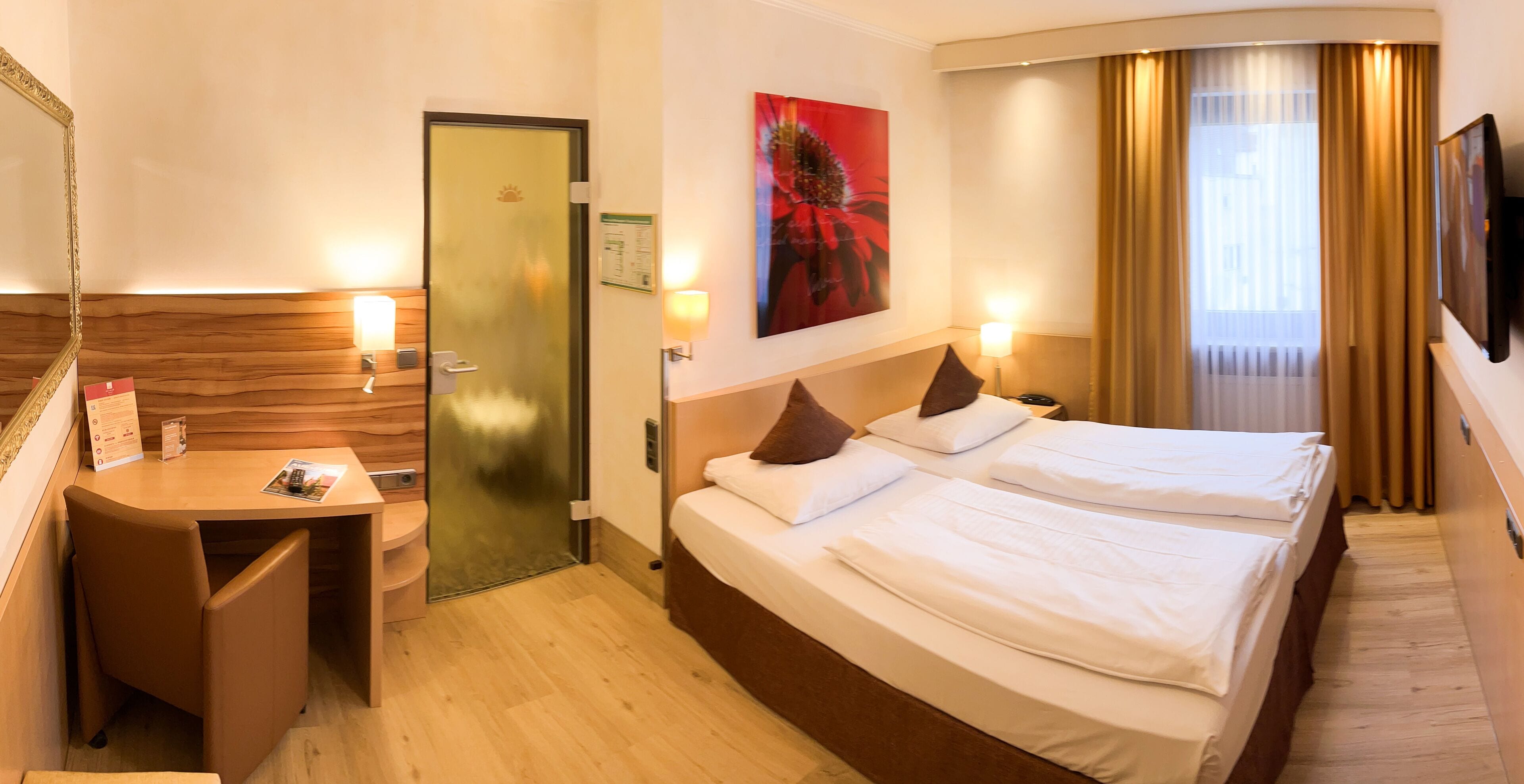 Habitación de hotel con dos camas, un escritorio, un espejo, una puerta y un cuadro.