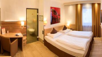 A hotel room with two beds, a desk, a mirror, a door, and a painting.