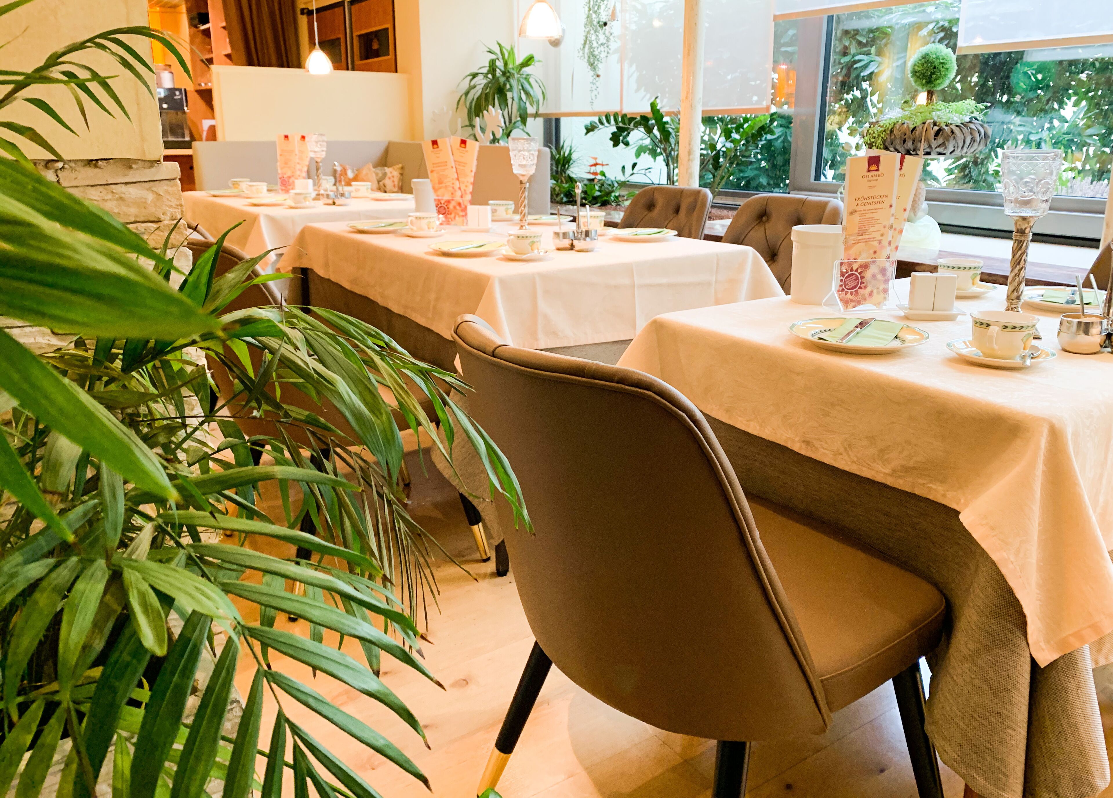 A restaurant with tables set for dining, chairs, and a large potted plant.