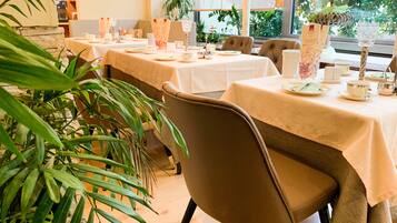 Un restaurante con mesas dispuestas para comer, sillas y una gran planta en maceta.