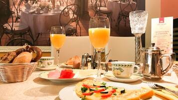 A breakfast setting with a croissant, a plate of vegetables, two glasses of orange juice, a basket of bread, and a coffee pot.