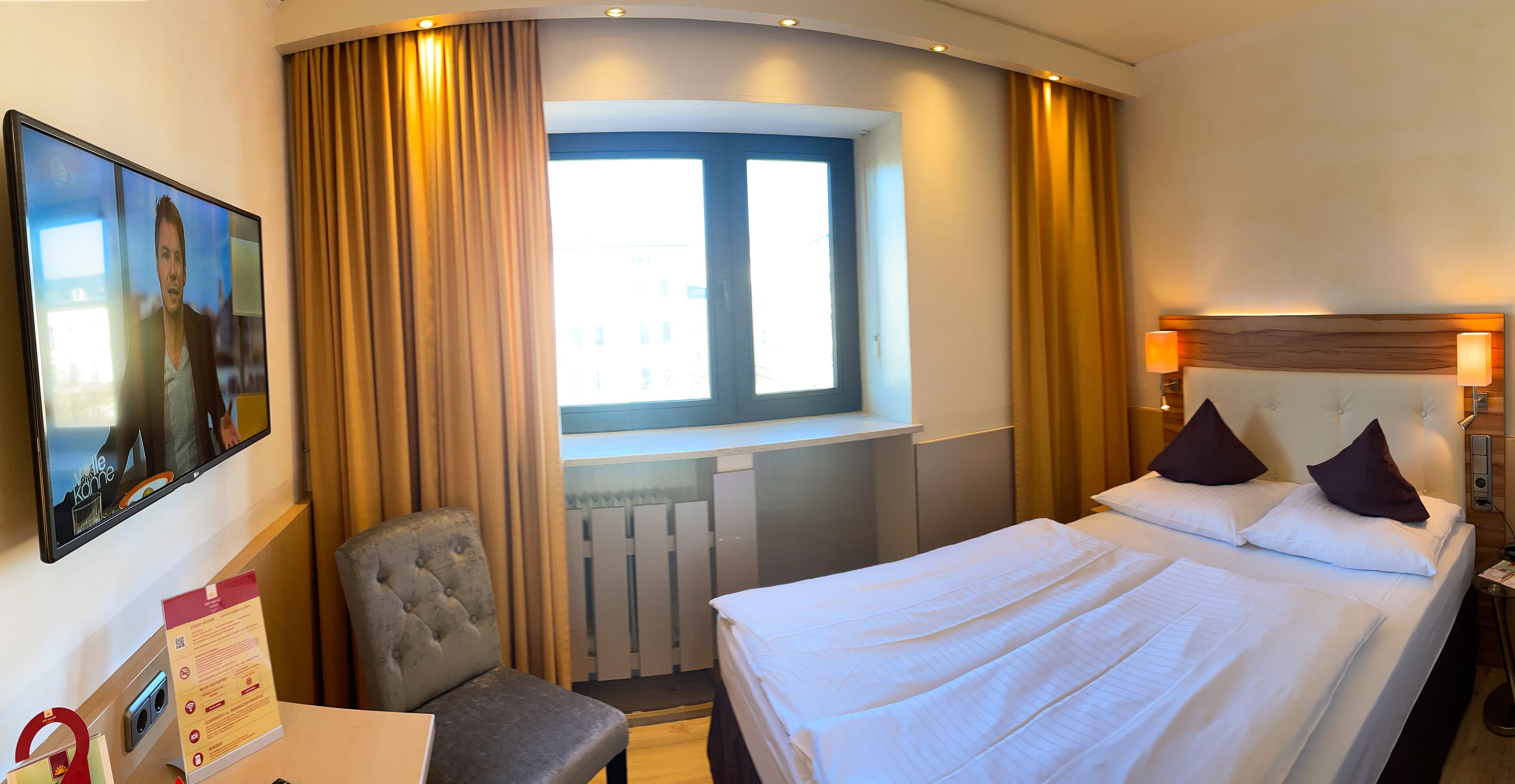 Una habitación de hotel con una cama, una silla, un escritorio, un ventanal y un televisor.