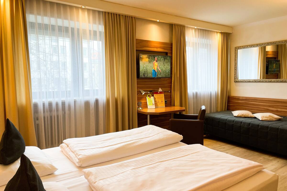 A hotel room with two beds, a desk with a TV, and a large mirror.