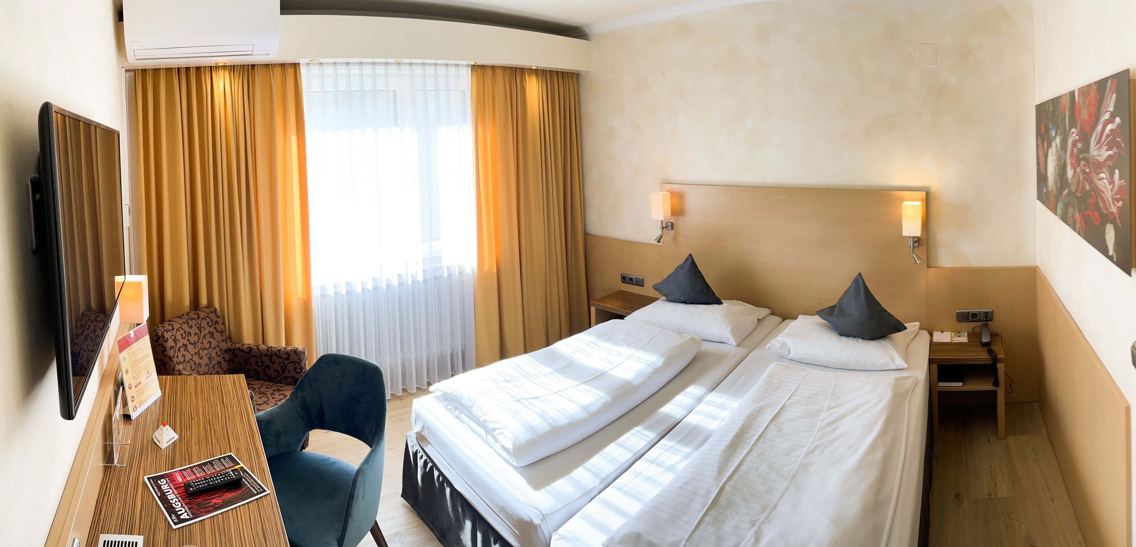 Habitación de hotel con dos camas, un escritorio con silla, televisión y un cuadro en la pared.
