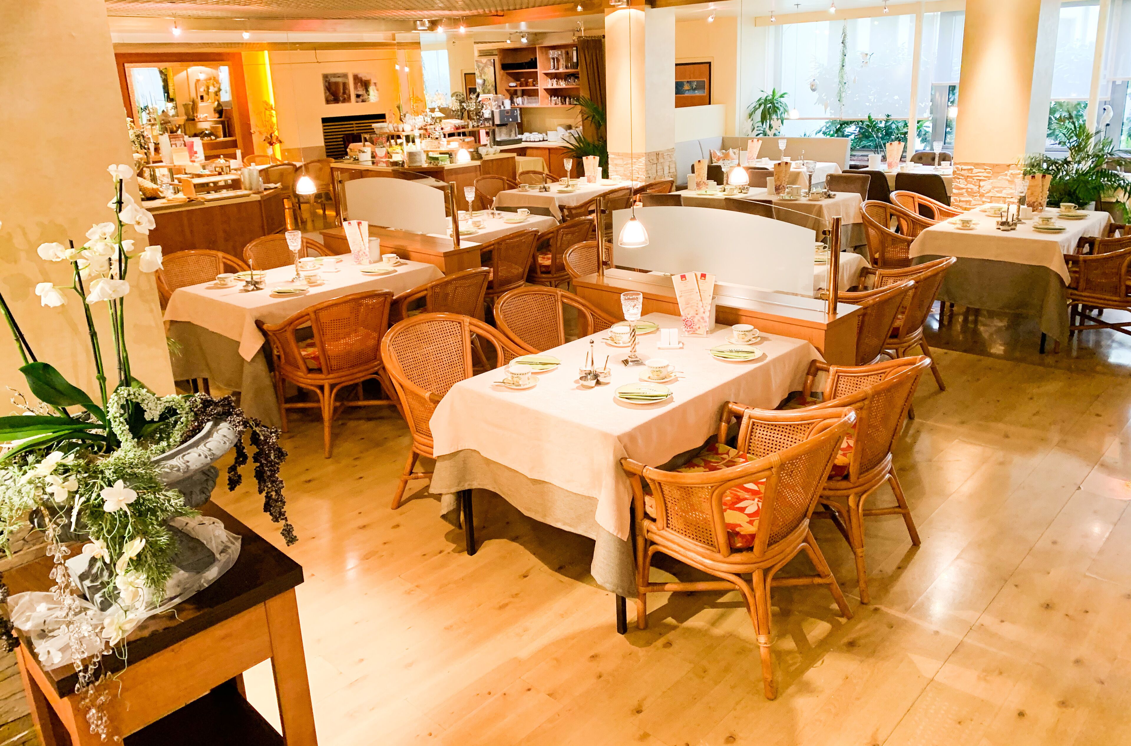 Ein Restaurant mit mehreren Tischen und Korbstühlen, das durch eine übersichtliche und aufgeräumte Gestaltung besticht.