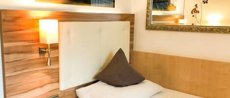 A hotel room with a bed, a bedside lamp, a telephone, a wall-mounted mirror, and a painting above the bed.