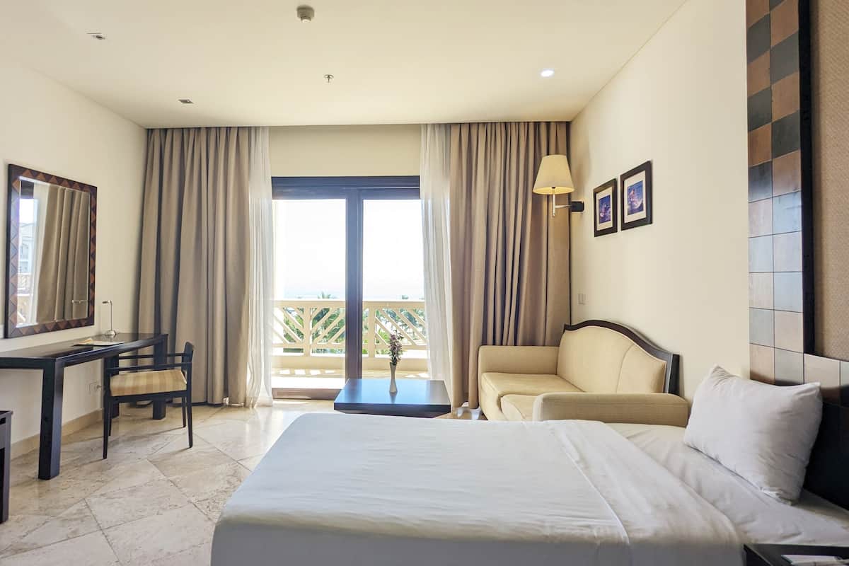 Une chambre d’hôtel comprenant un lit, un bureau, une chaise, un canapé, un balcon avec des rideaux et une vue sur l’extérieur.