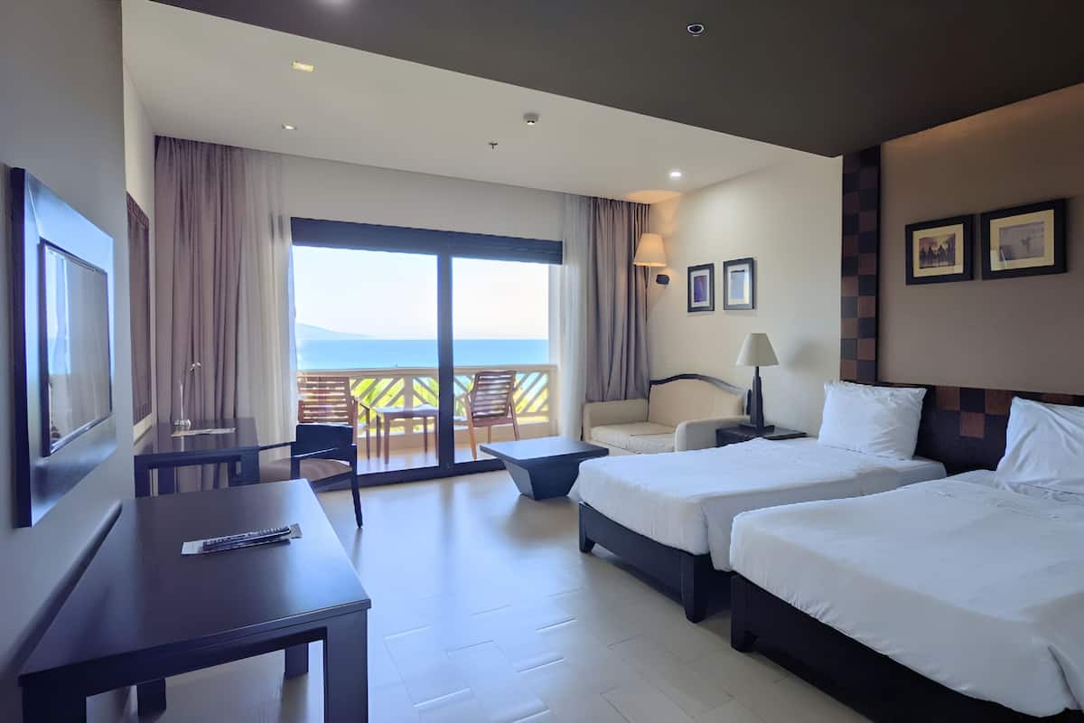 Une chambre d’hôtel avec deux lits, un bureau, une chaise, une télévision et un balcon avec vue.