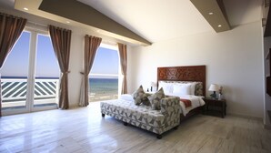 Quarto com cama, sofá, mesa de cabeceira e vista para a praia.