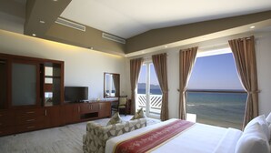 Quarto de hotel com uma cama grande, uma escrivaninha com televisão e vista para o mar.