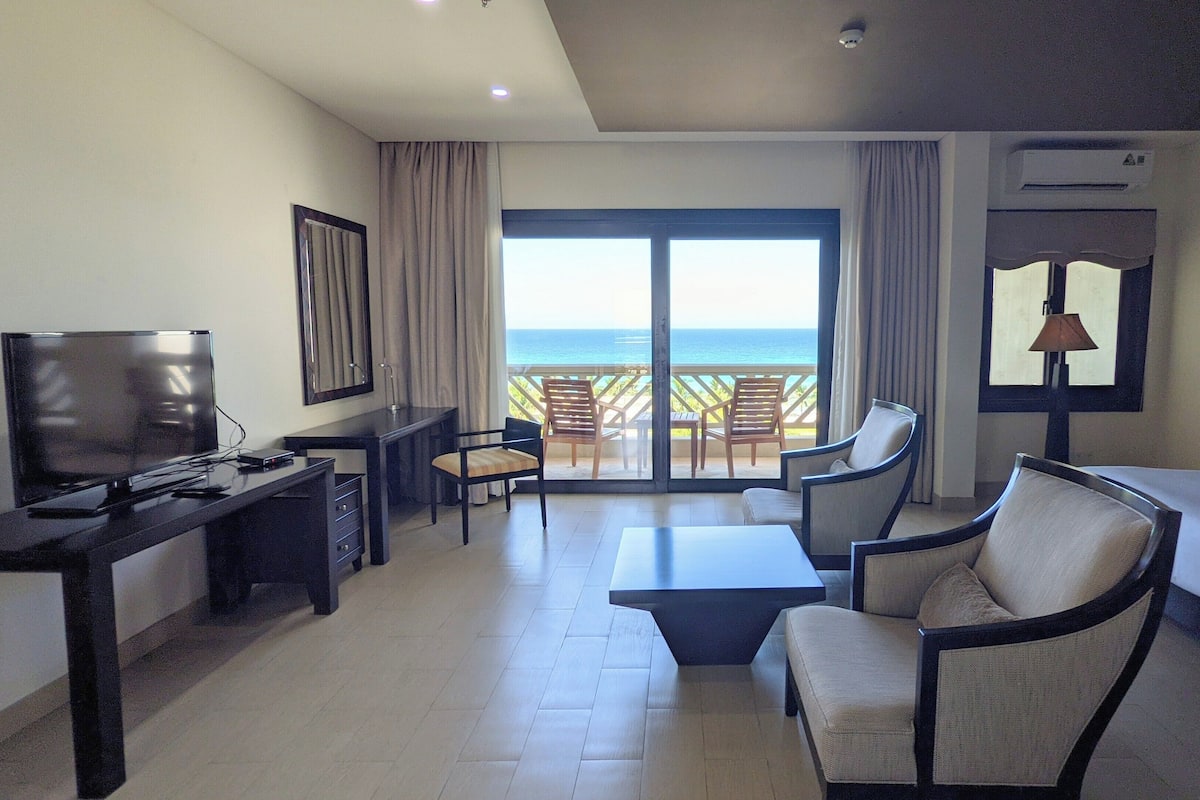 Une chambre d’hôtel avec un balcon, une télévision, un bureau, un lit et deux chaises.