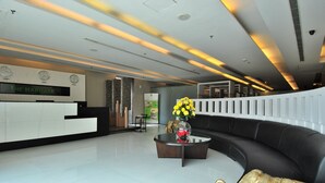 Un moderno vestíbulo de hotel con una recepción, un sofá negro, una mesa de centro con flores y una escultura decorativa de elefante.