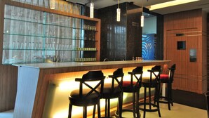 Zona de bar moderna con una vitrina de copas y botellas de vino, mostrador de bar de madera y taburetes negros.