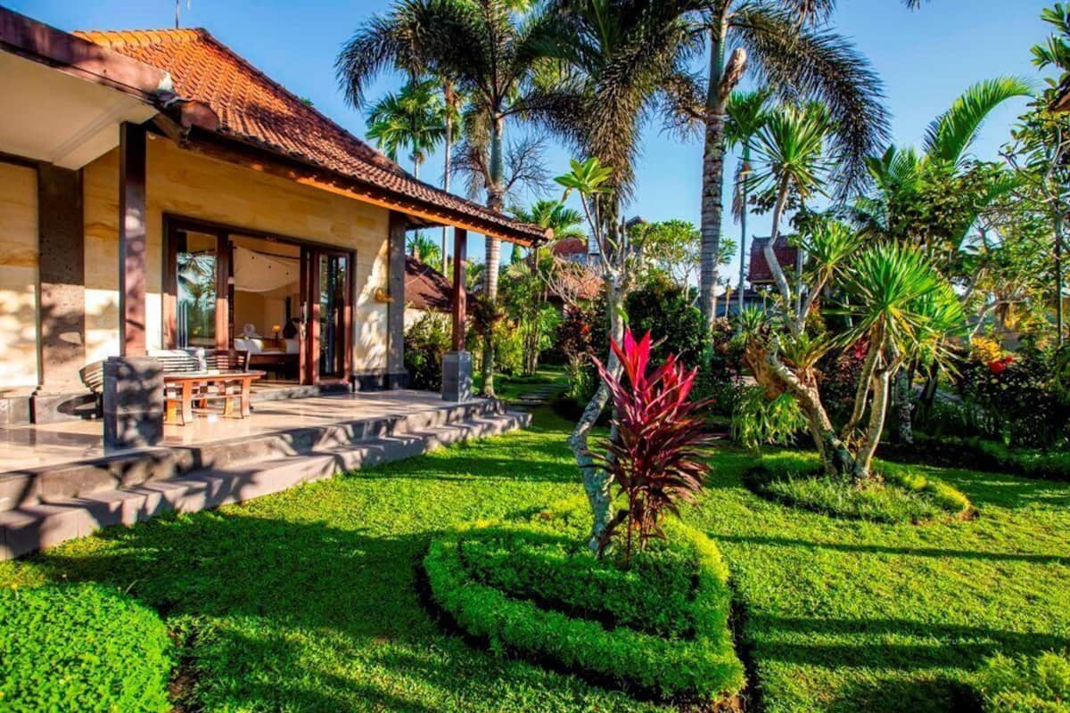 Un edificio de estilo tropical con techo de tejas, zona de estar cubierta al aire libre y jardines bien cuidados con palmeras y césped impecable.