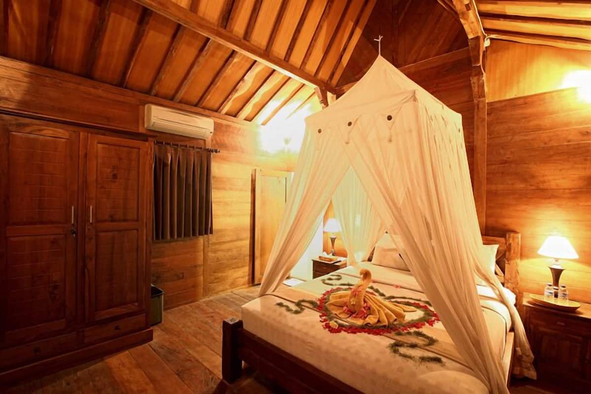 Una habitación de madera con una cama con dosel, paredes de madera y un ventilador de techo.