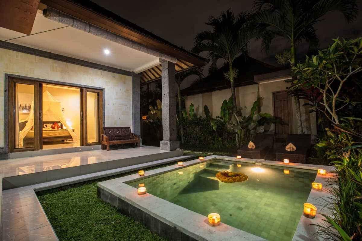 Una piscina con velas, un espacio de estar cubierto y un jardín con palmeras.