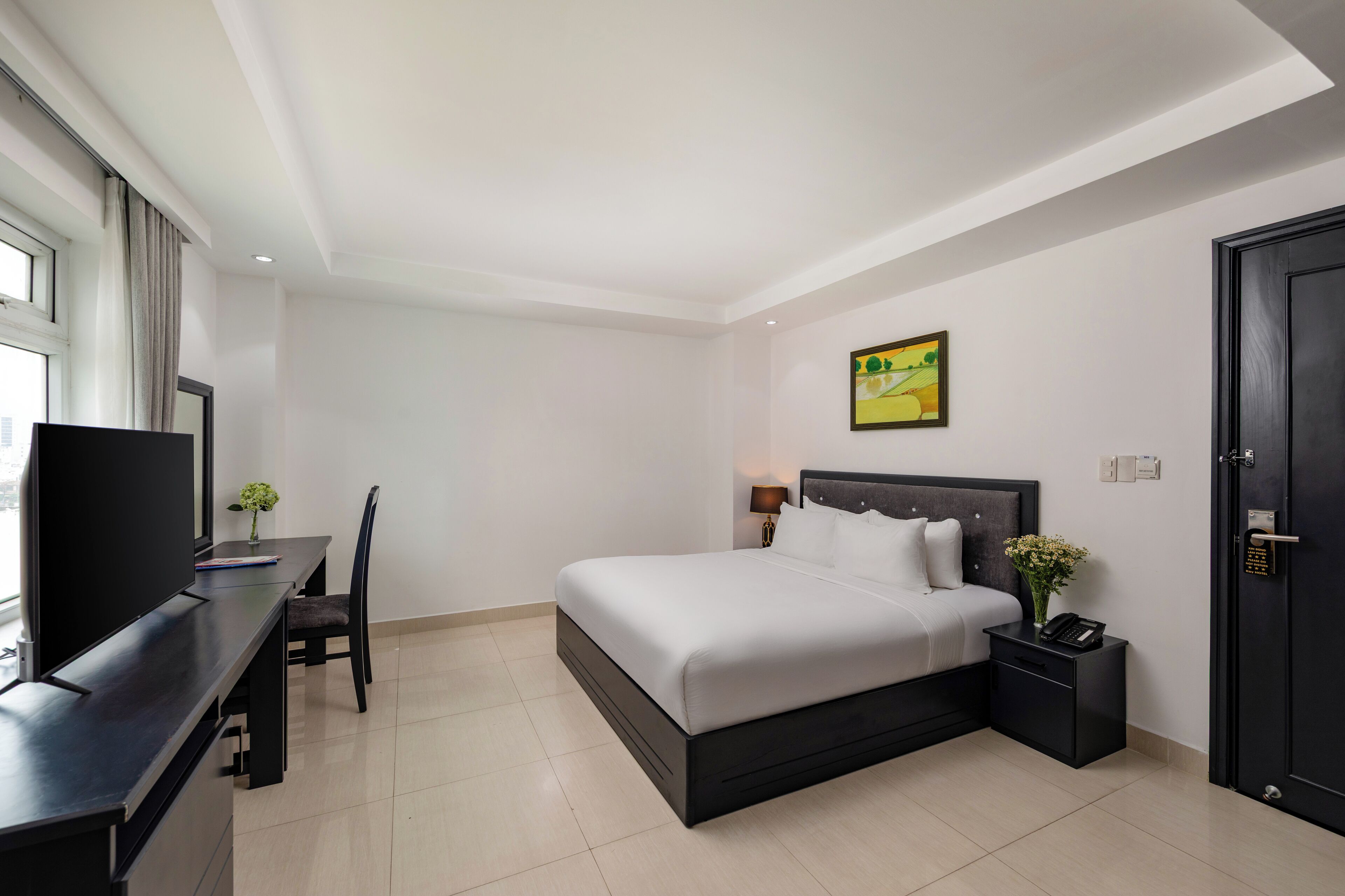 A hotel room with a bed, a desk with a chair, a TV, and a door.