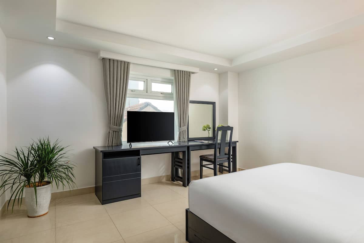 A modern hotel room with a large bed, a desk with a flat-screen TV, a chair, and a potted plant.