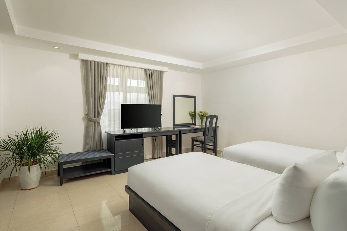 A modern hotel room with a bed, a desk with a TV, a chair, and a potted plant.