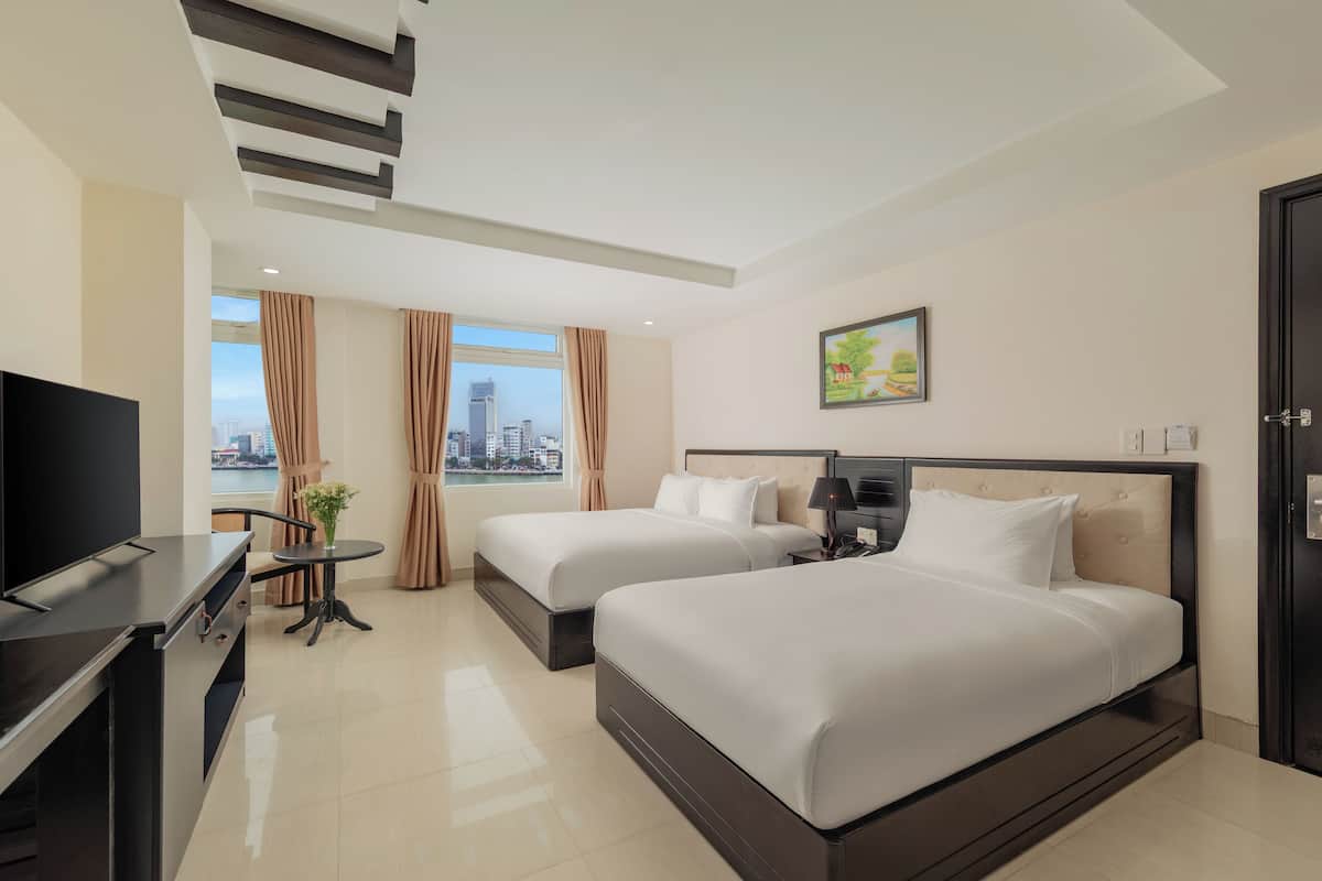 A hotel room with two beds, a TV, a small table with a vase, and a city view.