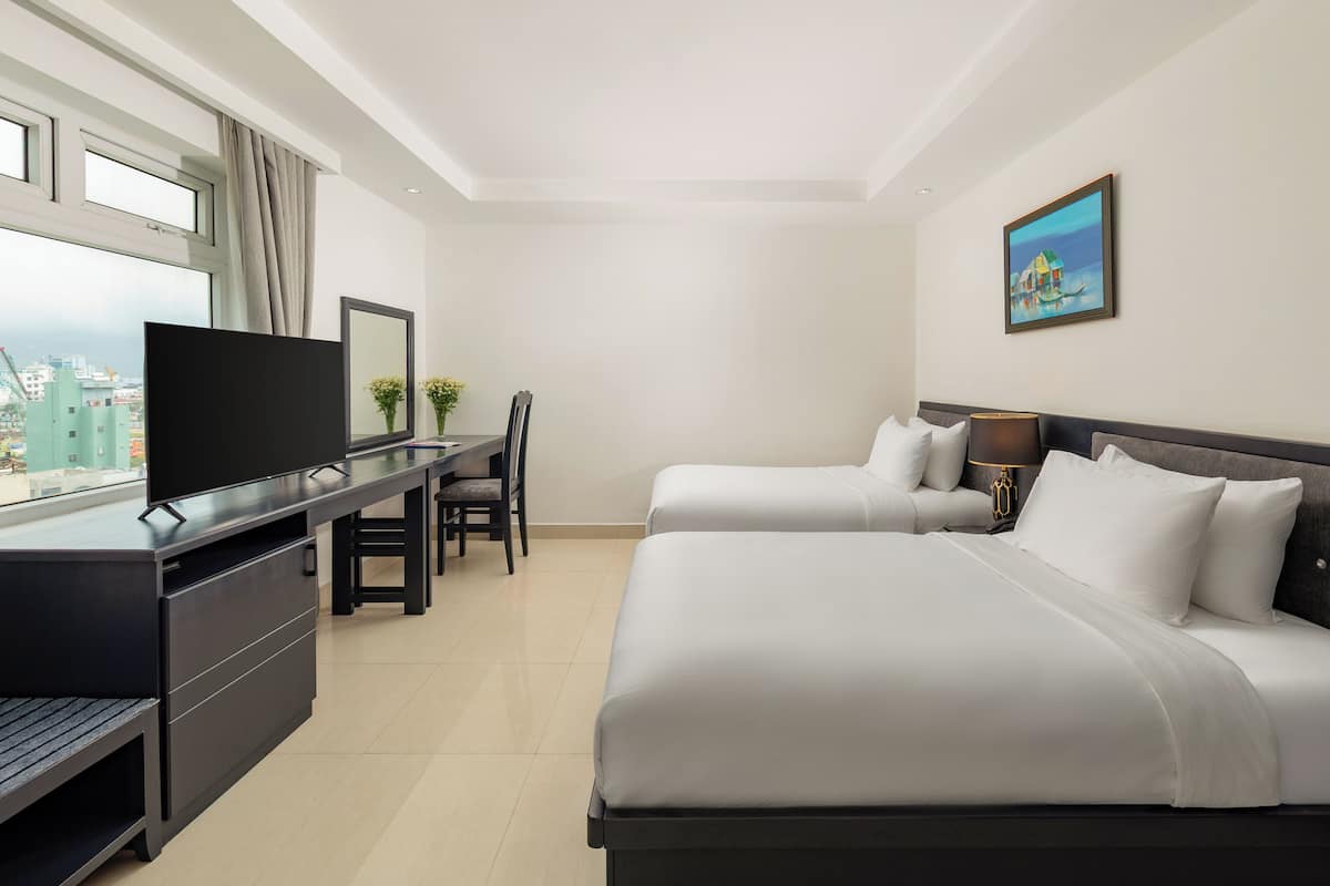 A hotel room with a bed, a desk, a chair, a TV, and a painting on the wall.