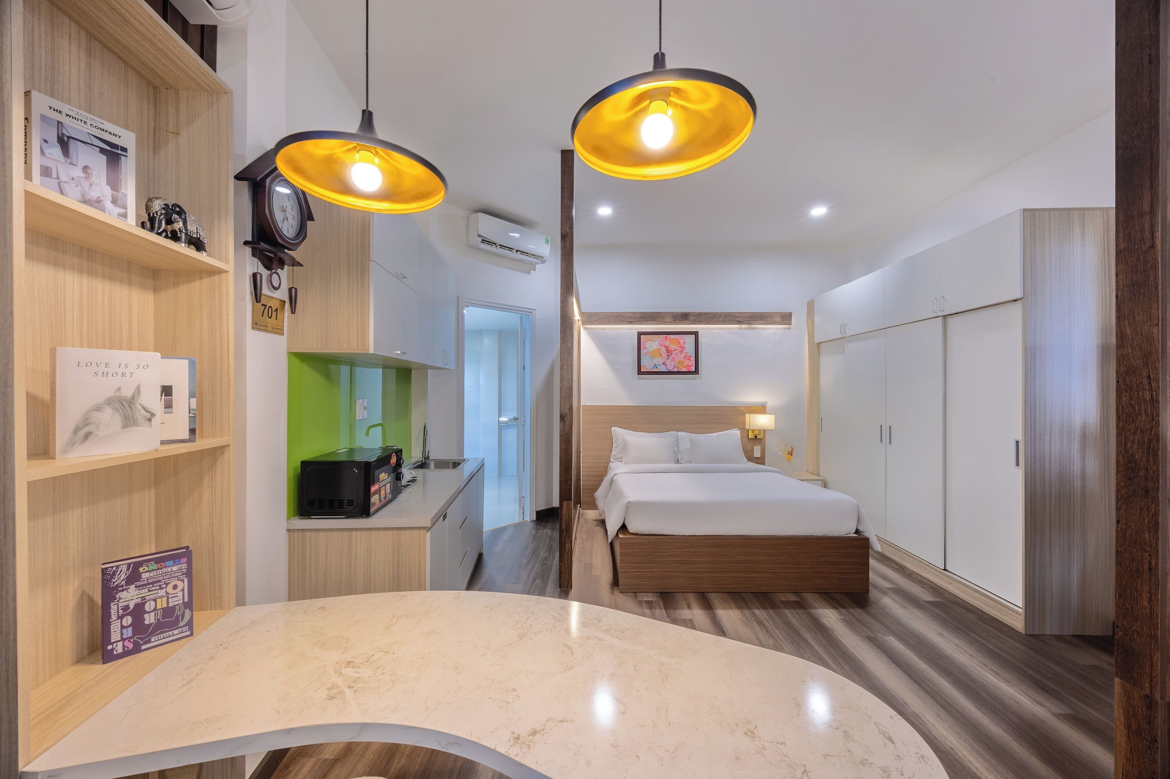 A modern hotel room with a curved marble countertop, a wooden bed, a desk with a computer, and a green wall.