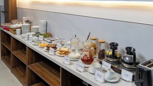 A buffet setup with various food items and beverages, including labeled containers for different dishes and a coffee machine. - A25 Hotel - 14 Pho Duc Chinh (Ho Chi Minh City)