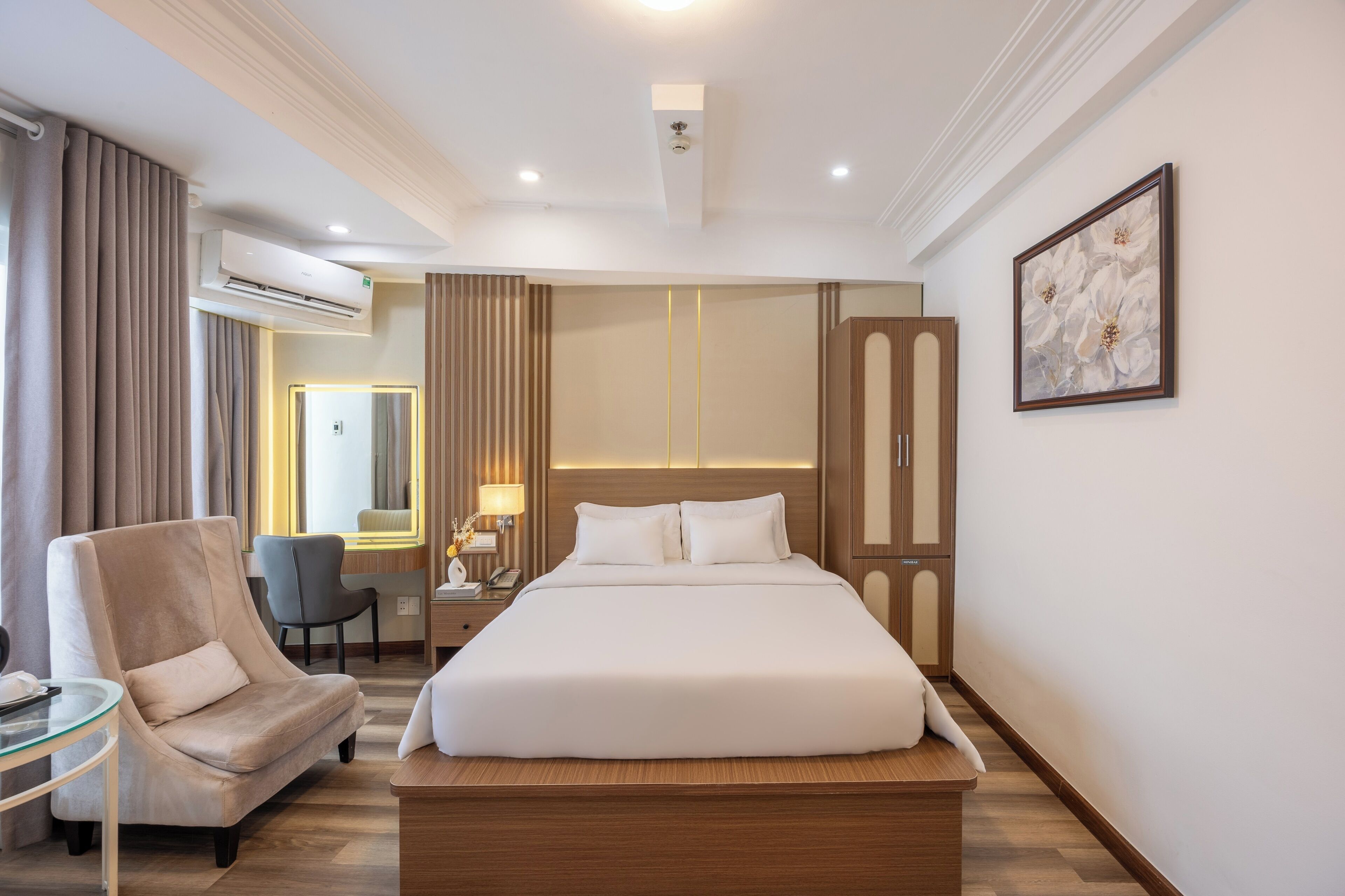 Habitación de hotel con una cama grande, una silla, un escritorio, un equipo de aire acondicionado y un cuadro en la pared.