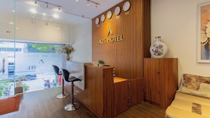 A reception desk with a wooden finish, a clock, and a vase with flowers. - A25 Hotel - 14 Pho Duc Chinh (Ho Chi Minh City)