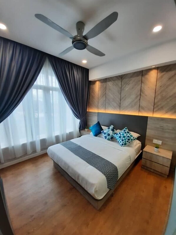 A modern bedroom with a large bed, dark curtains, a ceiling fan, and a nightstand with a plant.