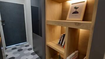 Un couloir doté d’un sol orné de motifs géométriques, une étagère en bois remplie de livres et d’un tableau encadré, et une porte avec une clé dans la serrure.