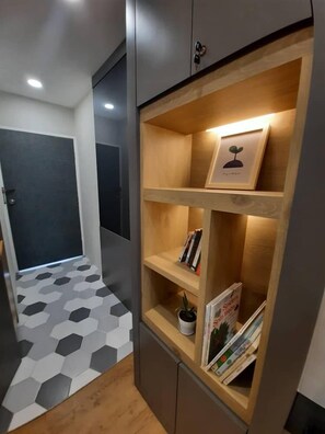 A hallway with a geometric-patterned floor, a wooden shelf unit with books and a framed picture, and a door with a key in the lock.