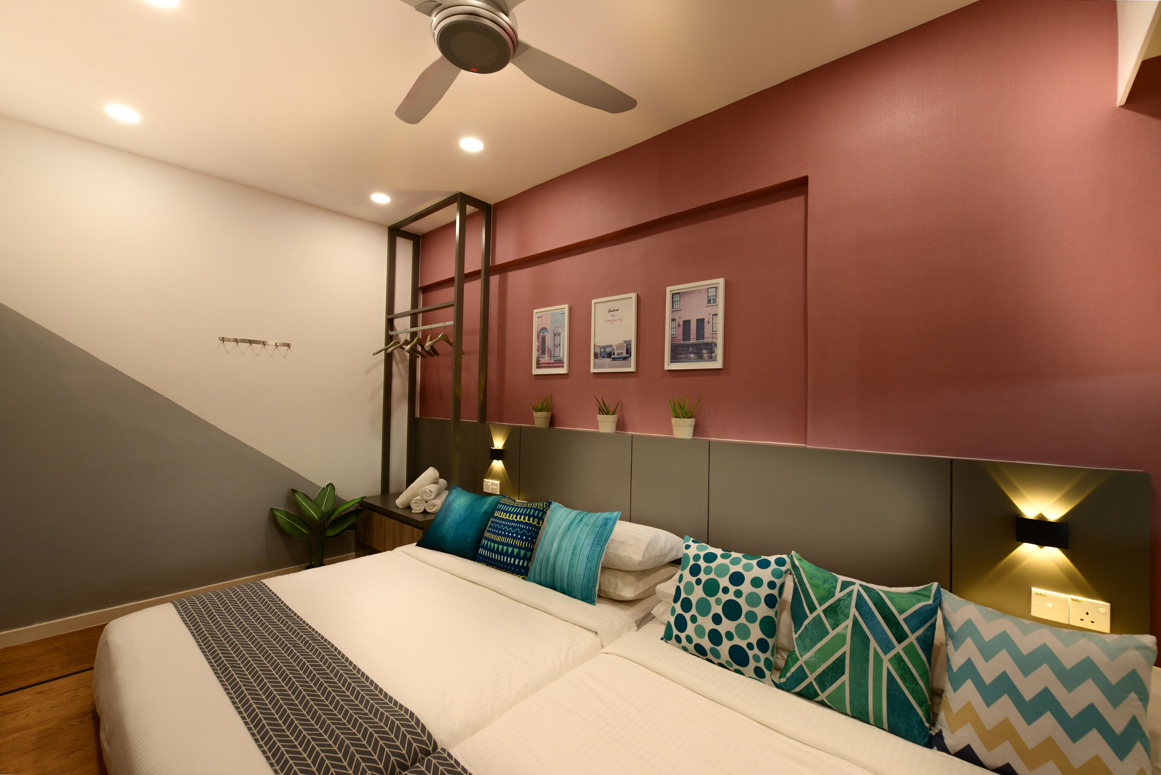 A modern bedroom with a bed, pillows, a ceiling fan, wall-mounted lights, and a small plant.