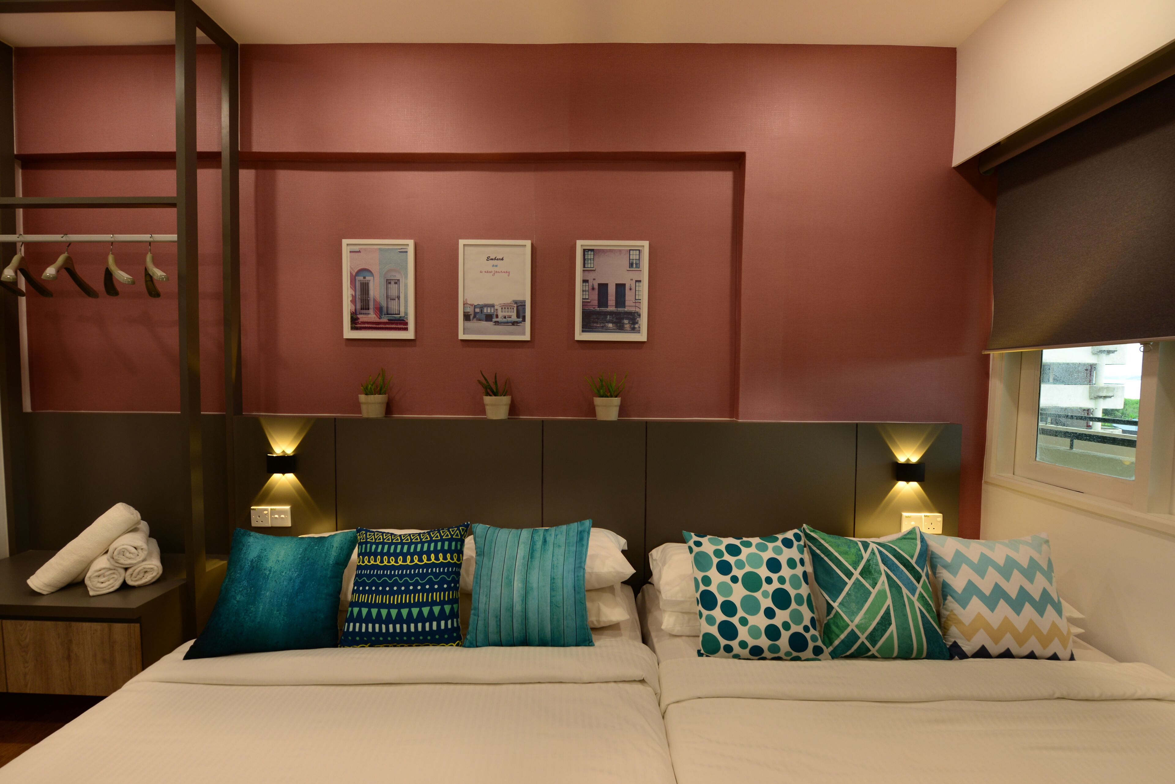 Een hotelkamer met een bed, kussens, wandlampen en ingelijste foto's.