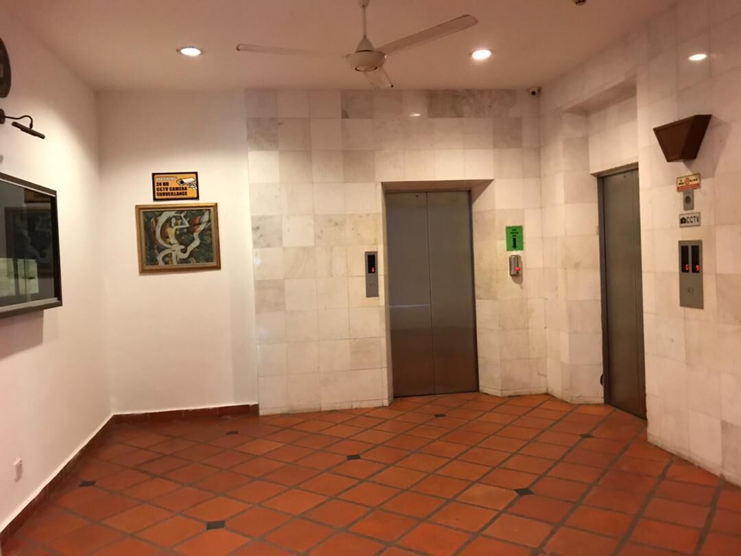 Zona de ascensor con suelo de baldosas, ventilador de techo y cámara de seguridad.