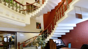 Un vaste hall d’entrée avec un sol en marbre, un escalier aux accents rouge et blanc, et un espace détente avec une table et des chaises à plateaux en verre.