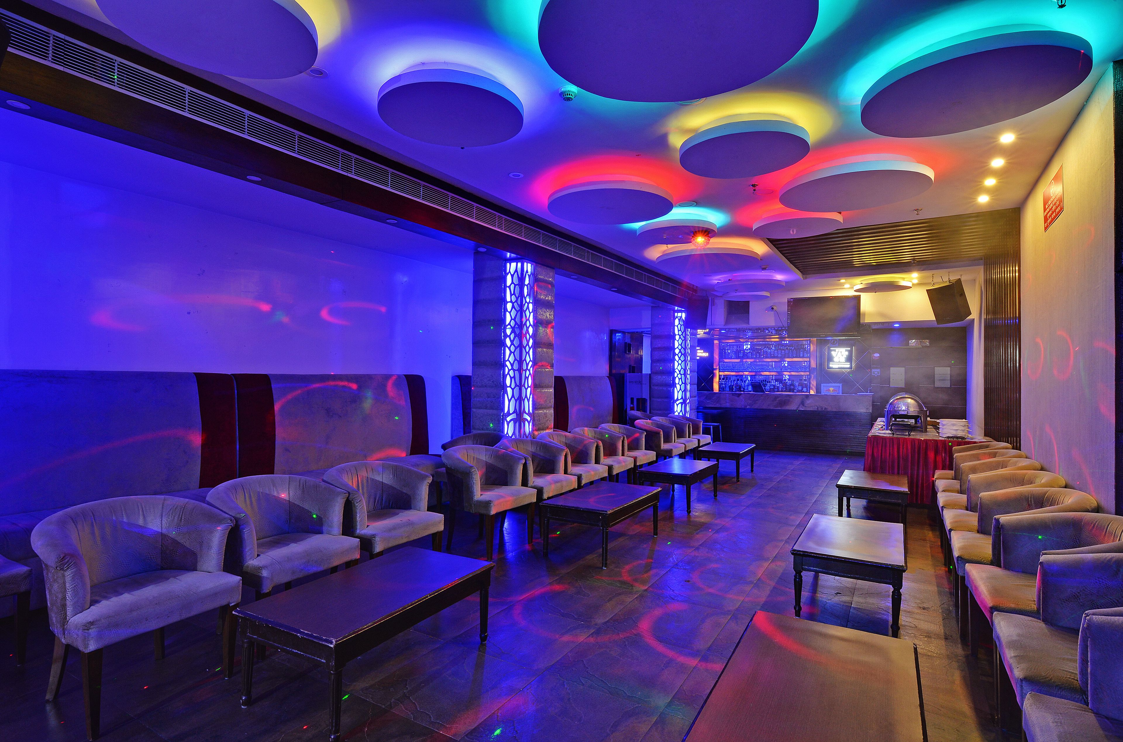 A lounge area with rows of chairs and tables, a bar area with a counter and stools, and a ceiling with circular light fixtures.
