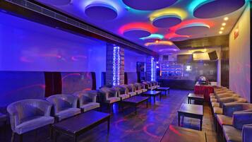 A lounge area with rows of chairs and tables, a bar area with a counter and stools, and a ceiling with circular light fixtures.