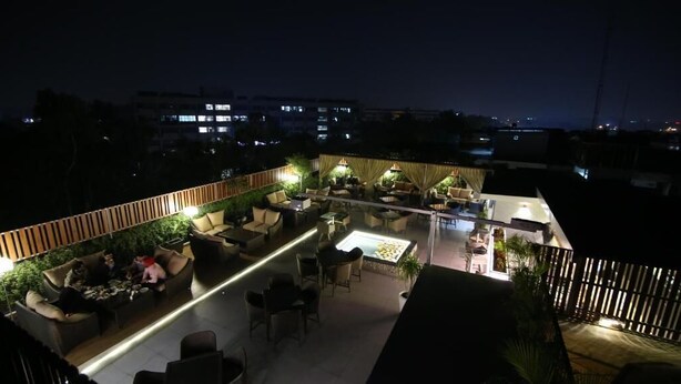 Un salon extérieur aménagé sur le toit, avec des espaces pour s’asseoir, un éclairage d’ambiance et une vue sur le paysage urbain la nuit.