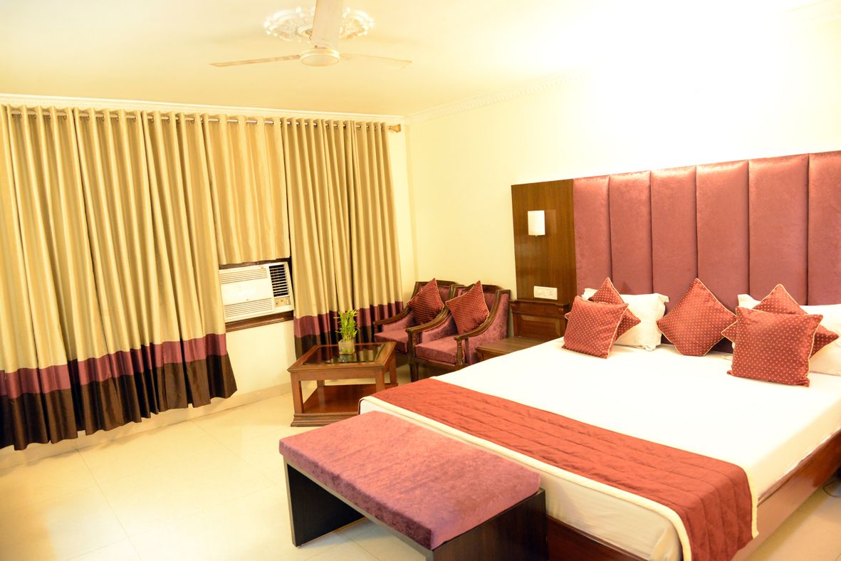 A hotel room with a large bed, a wooden headboard, a desk with a chair, and a window with curtains.
