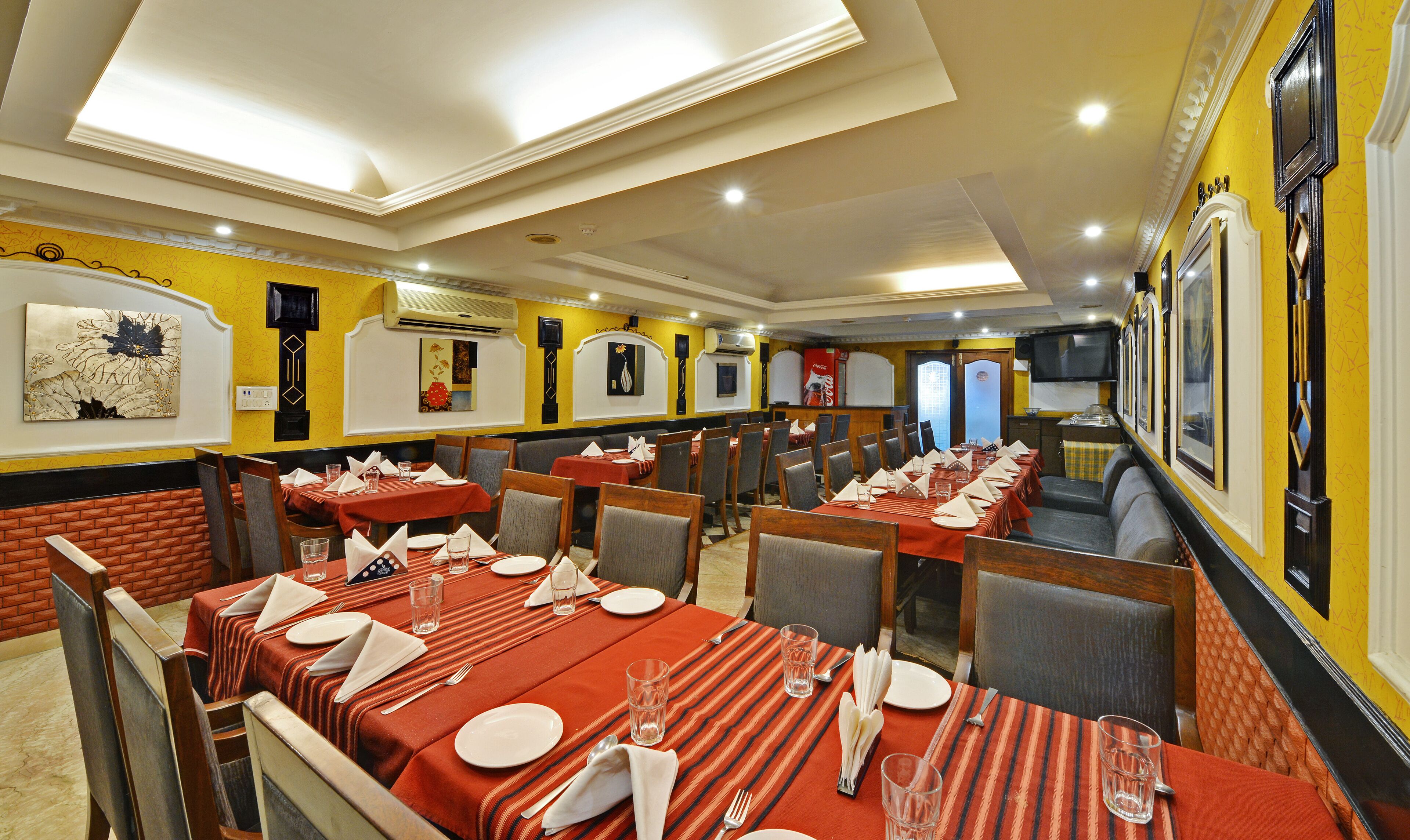 A restaurant with multiple tables set for dining, featuring a brick wall and yellow decor.