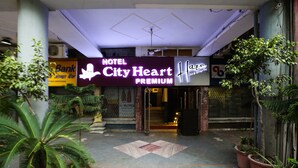 L’entrée de l’hôtel City Heart Premium, avec son panneau indicateur, ses plantes en pot et son sol carrelé.