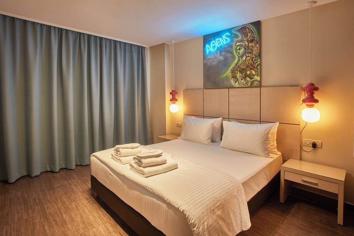 A hotel room with a large bed, two bedside tables, a wall-mounted artwork, and a window with curtains.