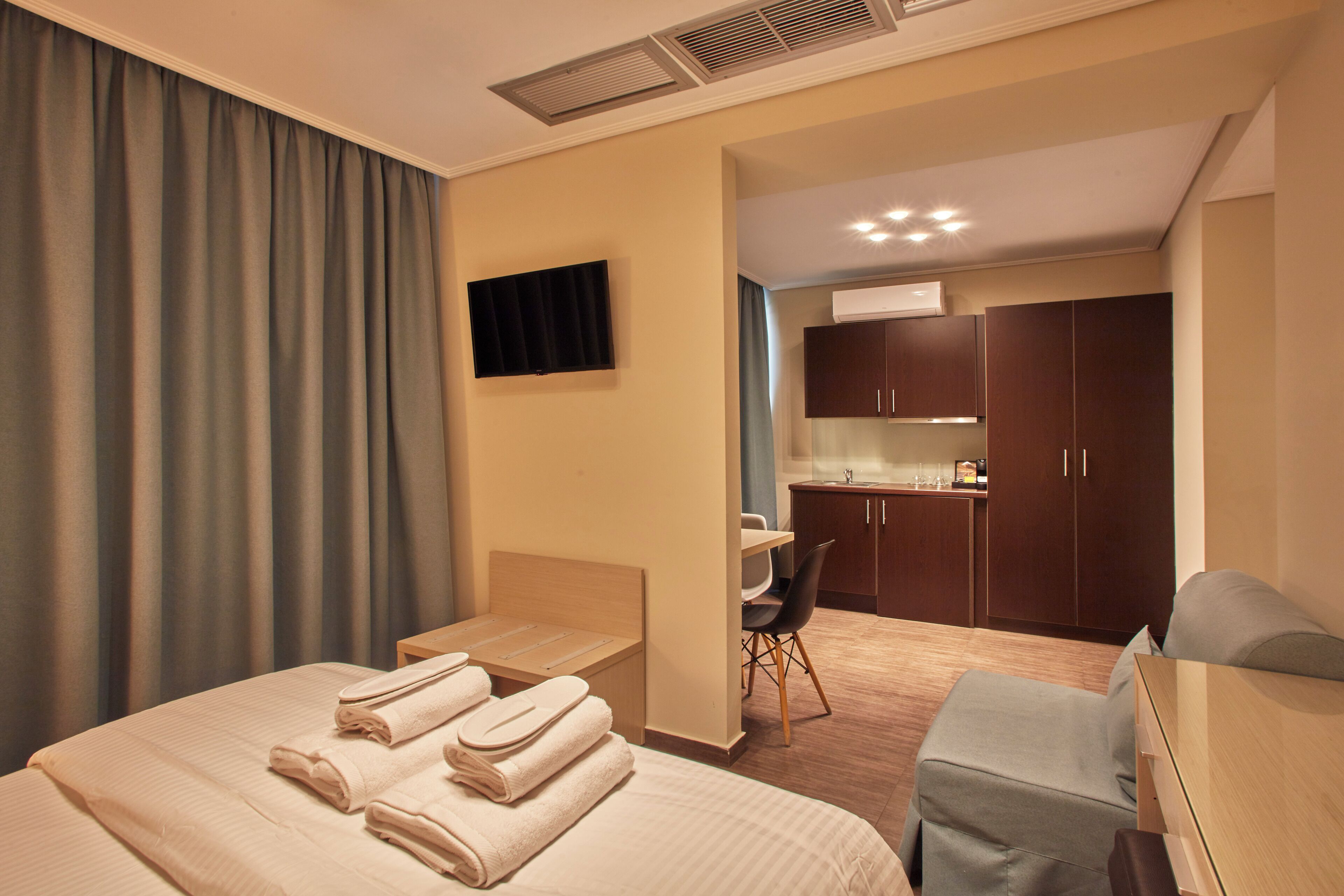 A hotel room with a bed, a desk, a chair, a TV, and a kitchenette.