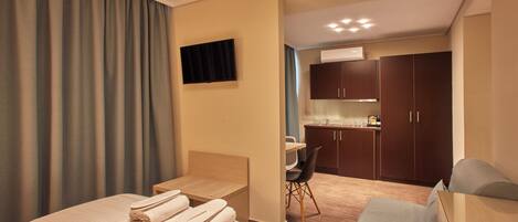 A hotel room with a bed, a desk, a chair, a TV, and a kitchenette.