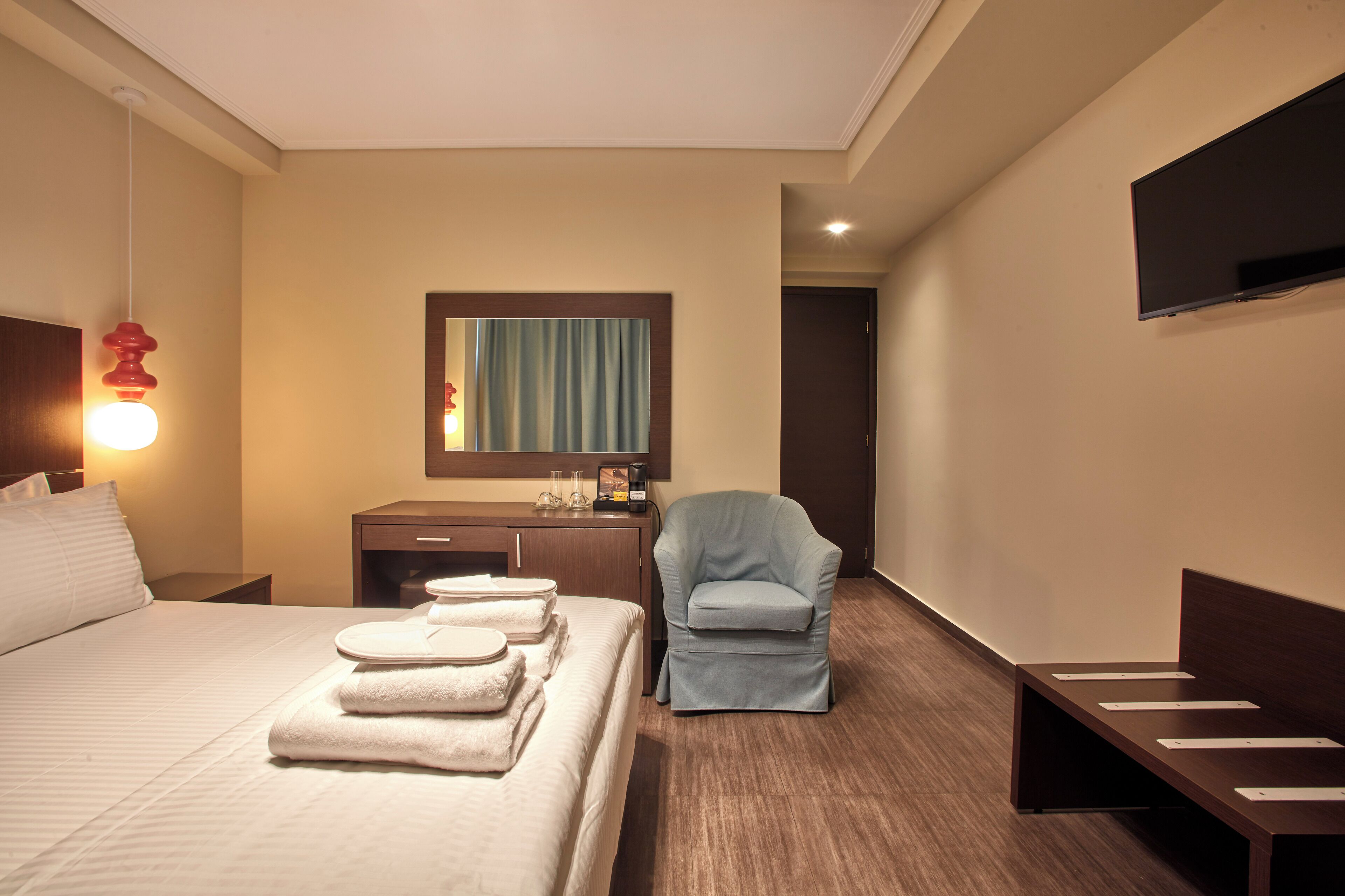 Una habitación de hotel con cama, escritorio, silla, televisor y espejo.