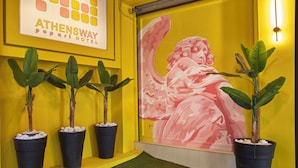 A hotel lobby with a yellow wall, a mural, potted plants, and a sign for 'ATHENSWAY POP ART HOTEL'. - Athens Way Pop Art Hotel (Athens)