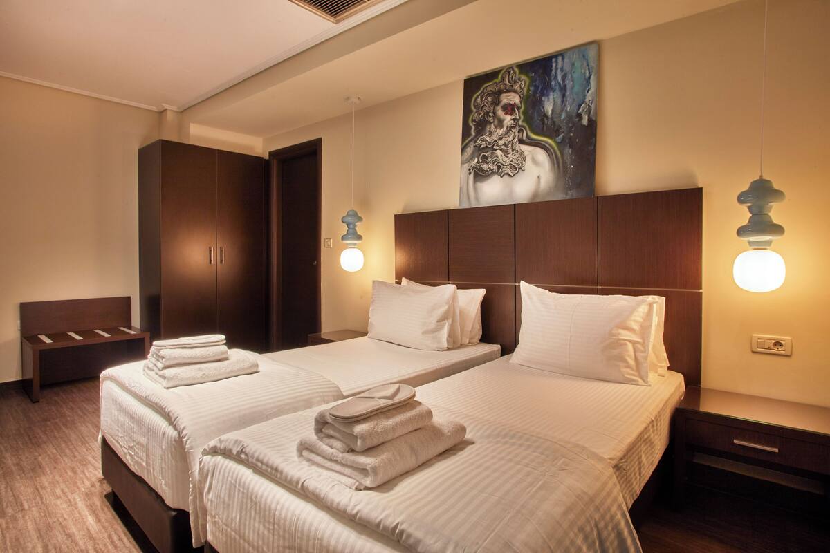 A hotel room with two beds, a bench, and a painting on the wall.