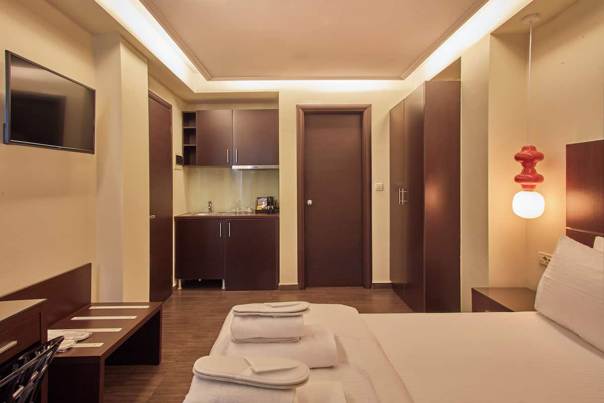 A hotel room with a bed, bedside tables, a TV, a small kitchenette, and a bathroom.