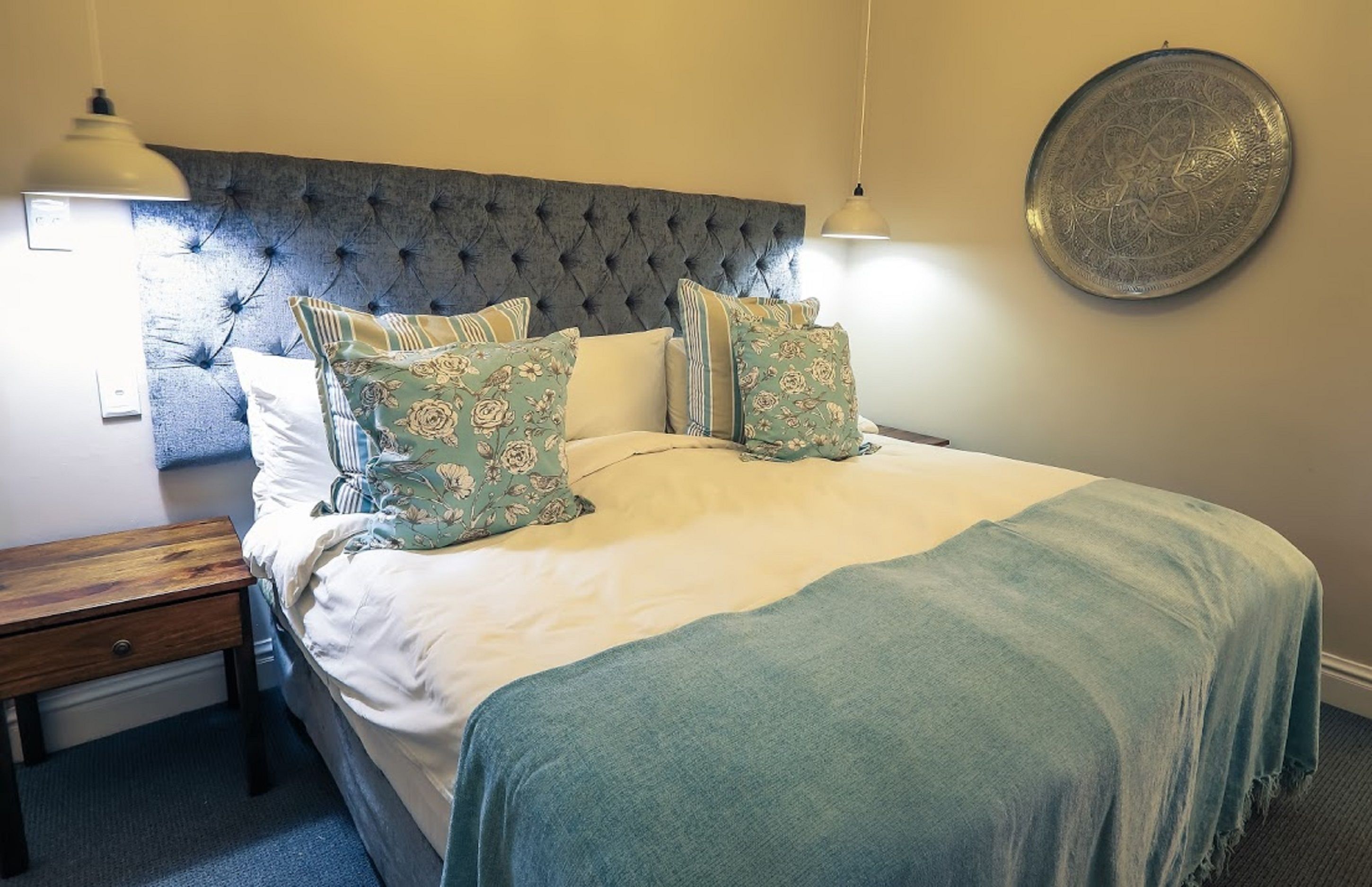 A neatly made bed with floral pillows, a tufted headboard, and a round decorative plate on the wall.